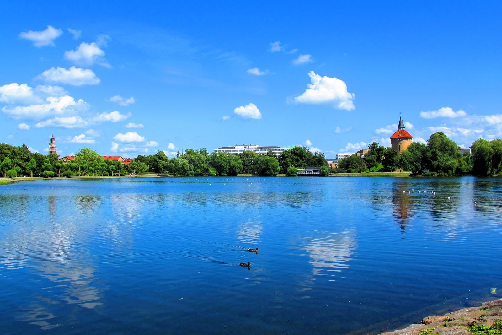 See in malerischer Landschaft mit Turm, blauer Himmel und reflektierendem Wasser.