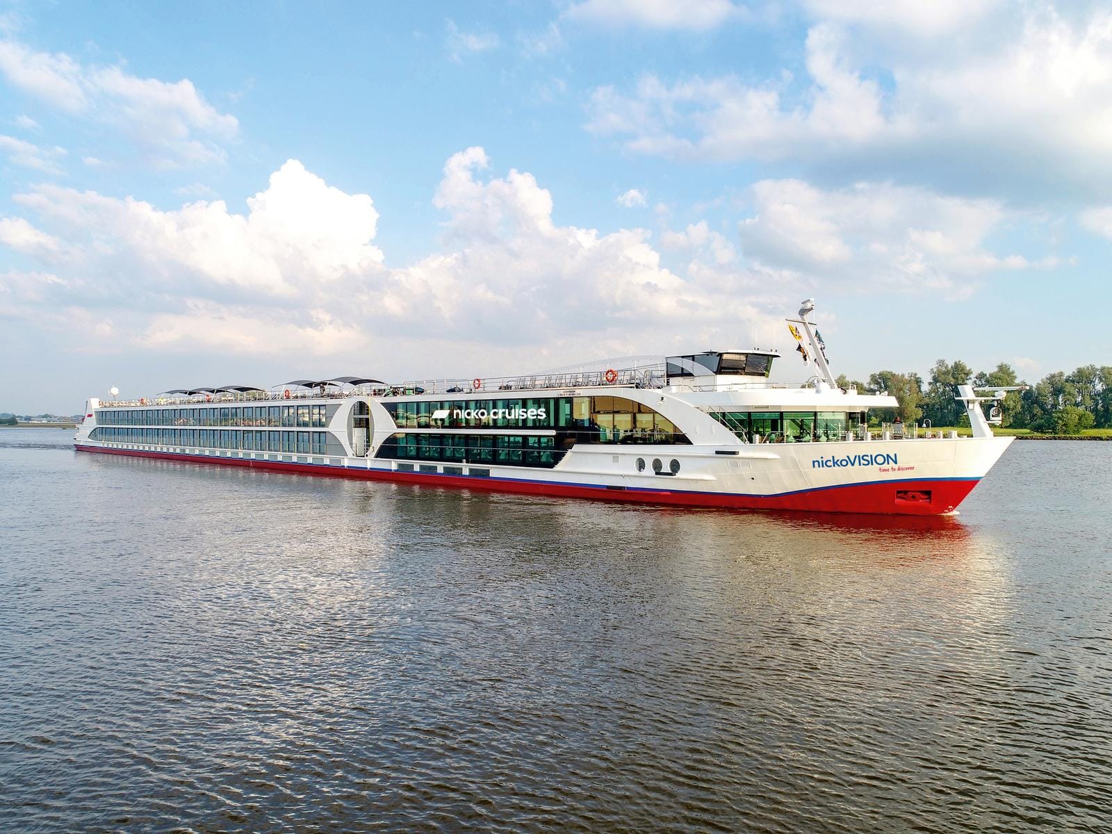 Flusskreuzfahrtschiff auf ruhigem Fluss unter blauem Himmel mit weißen Wolken.