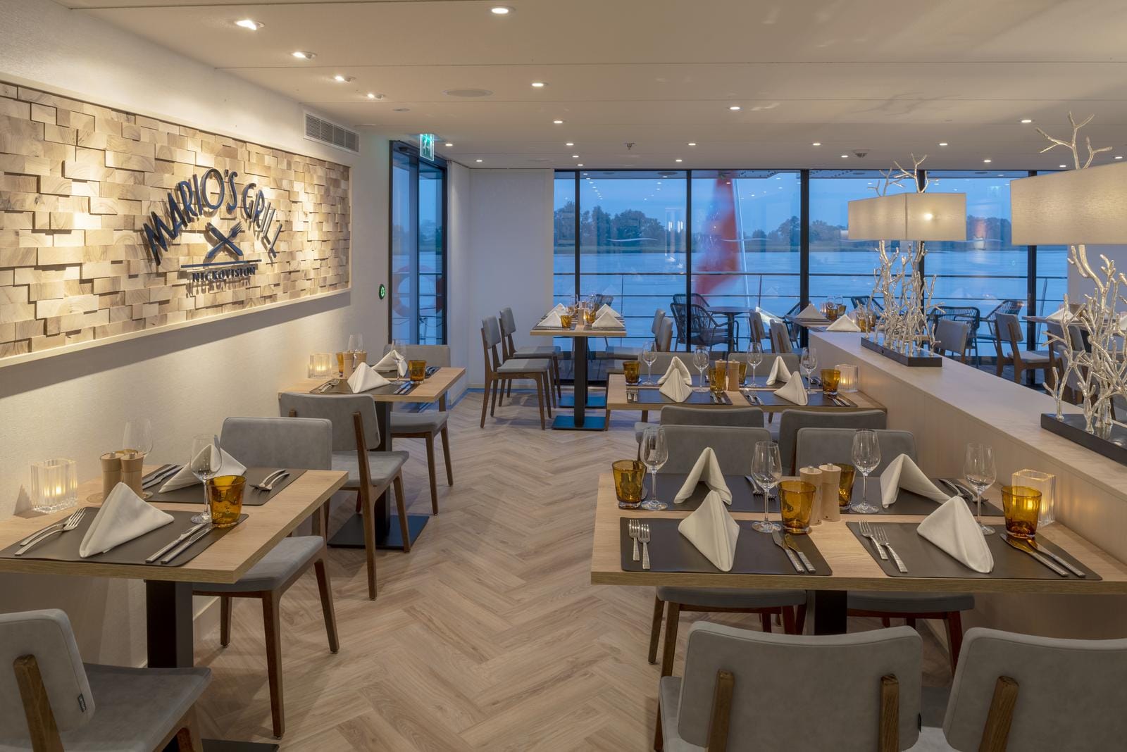 Modernes Hotelrestaurant mit Holzboden, eleganten Gedecken und Blick auf den Fluss.