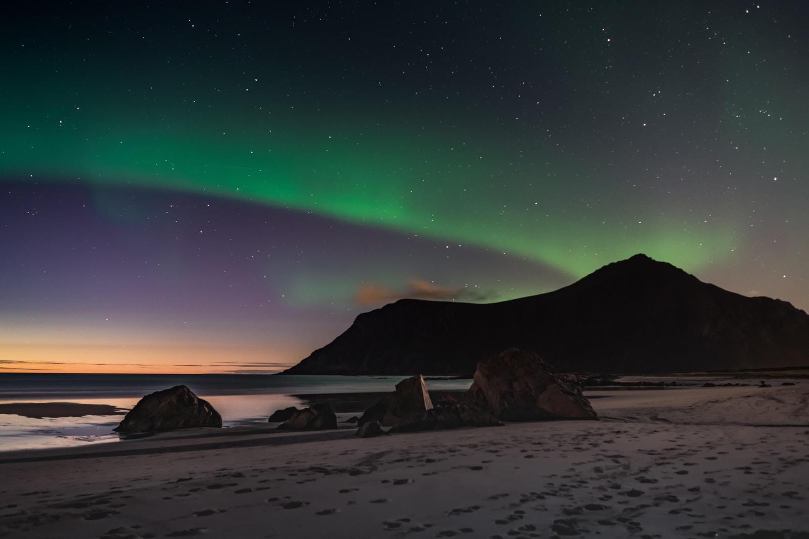 Nordlicht über einem Strand mit Bergen bei Nacht in Norwegen.