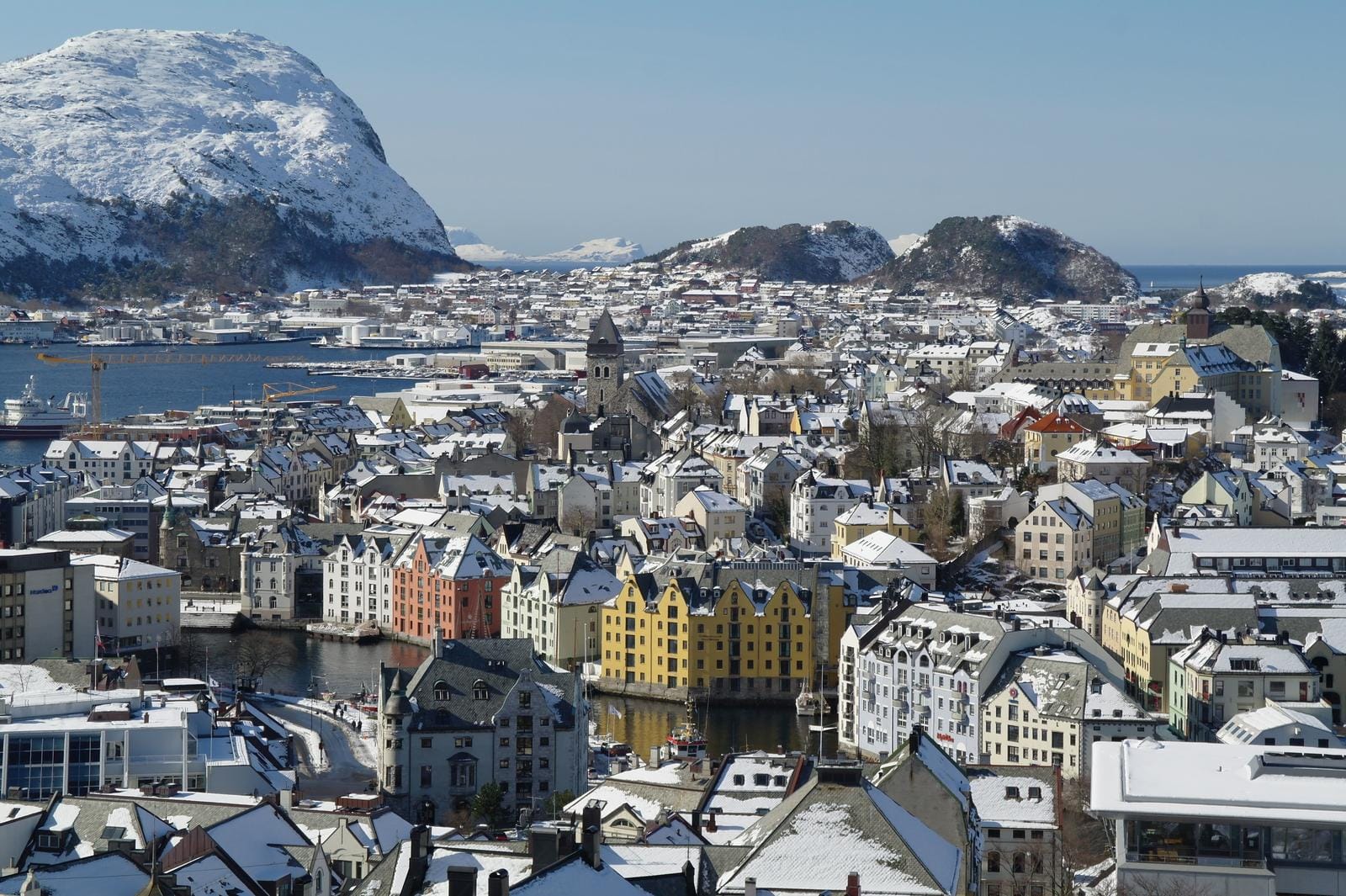 Verschneite Stadtansicht von Ålesund, Norwegen, mit bunten Häusern und umliegenden Bergen.
