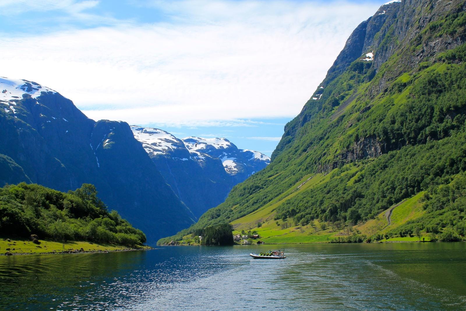 Norwegen, Fjordlandschaft mit grünen Hügeln, schneebedeckten Bergen und klarem Wasser.