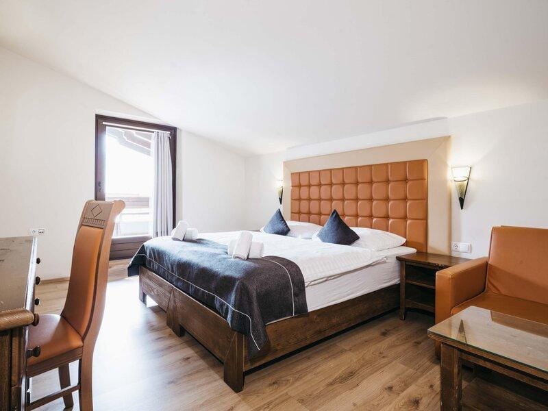 Gemütliches Hotelzimmer mit Doppelbett, Holzboden und Ledersessel in warmen Erdtönen.
