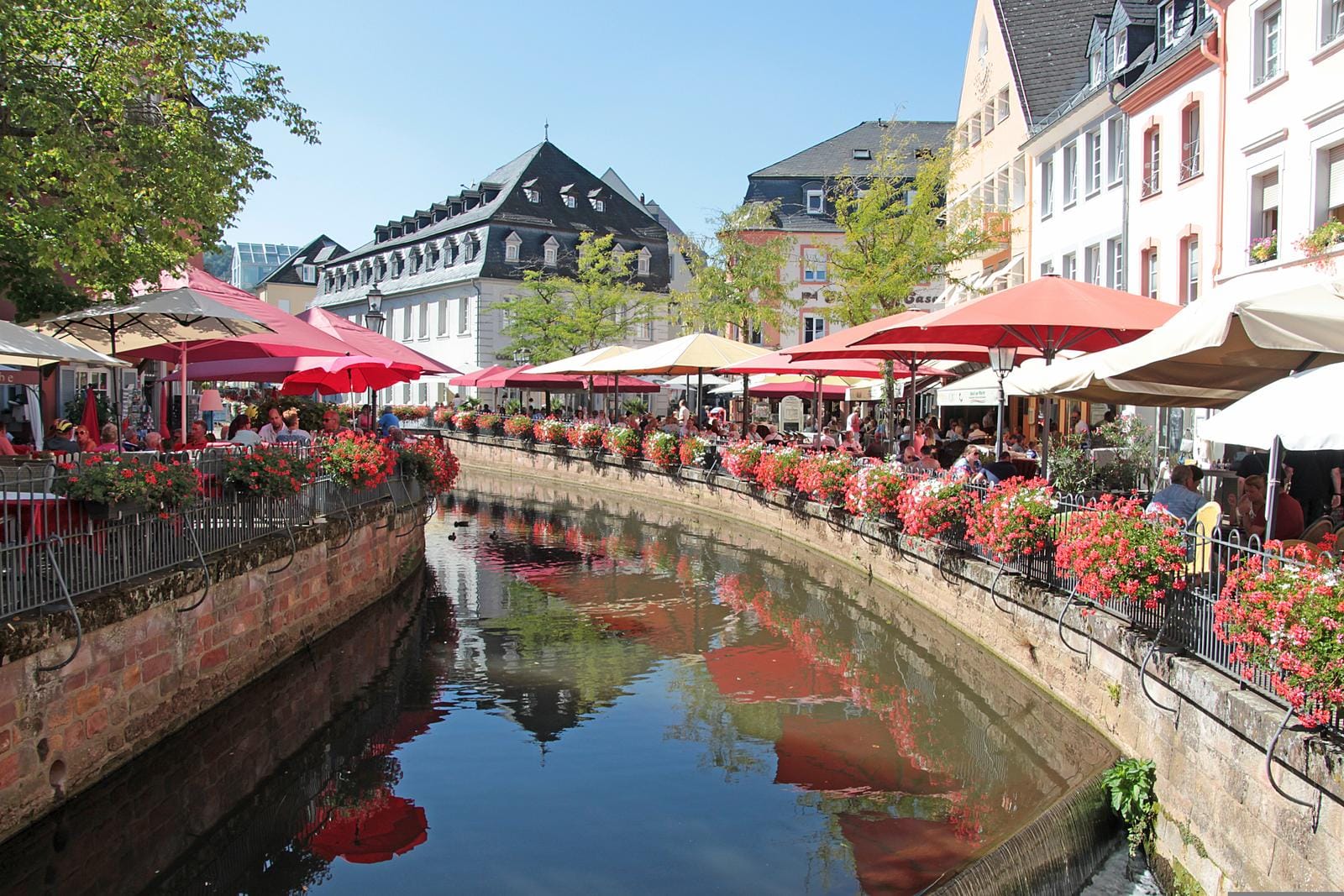 Malersicherer Kanal in Saarburg, Deutschland, mit blühenden Blumen und gemütlichen Cafés.