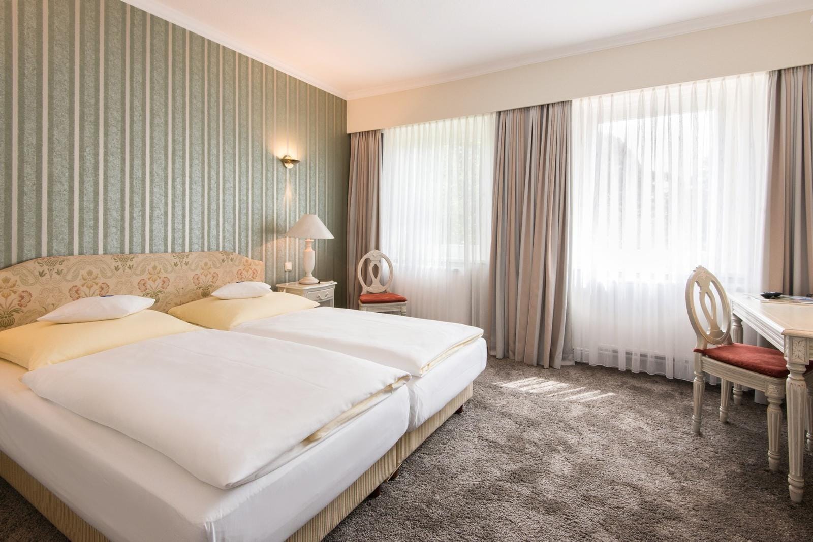 Gemütliches Hotelzimmer mit Doppelbett, klassischen Möbeln und sanften Grüntönen.