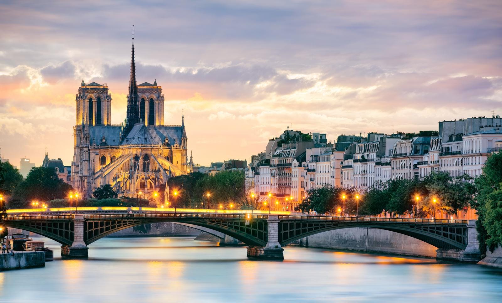 Notre-Dame bei Sonnenuntergang, Paris, mit erleuchteter Brücke und Wasser im Vordergrund.