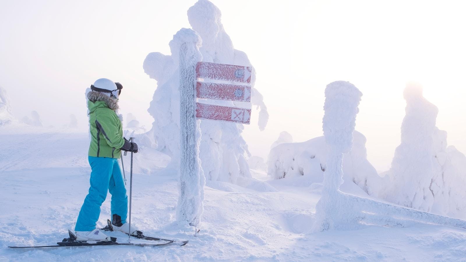 Verschneite Winterlandschaft in Lappland mit Skifahrer und vereistem Wegweiser.