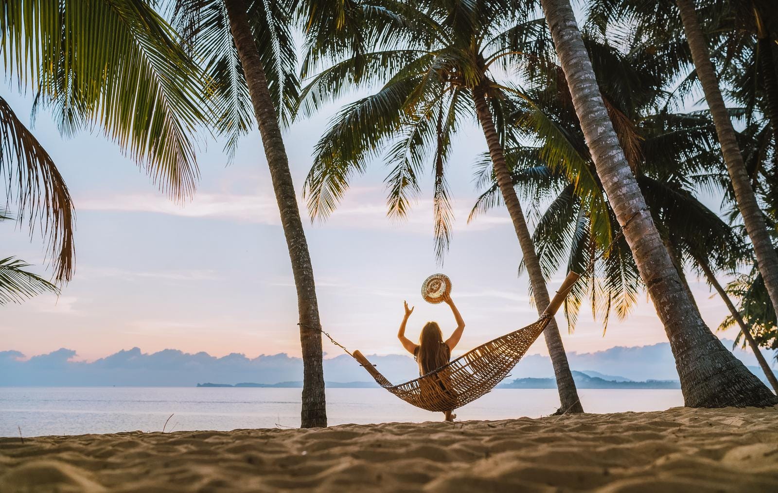 Frau in Hängematte unter Palmen am Strand bei Sonnenuntergang, entspannte Stimmung.