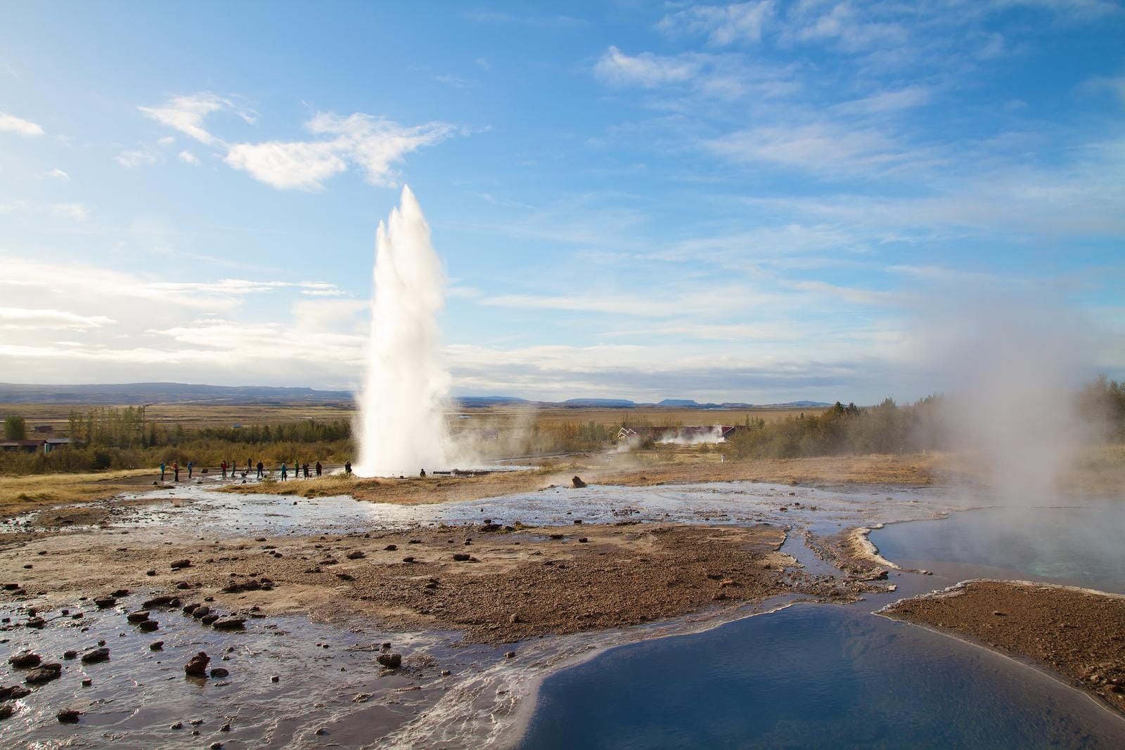 Geysir in Island, sprudelndes Wasser in weiter Landschaft unter blauem Himmel.