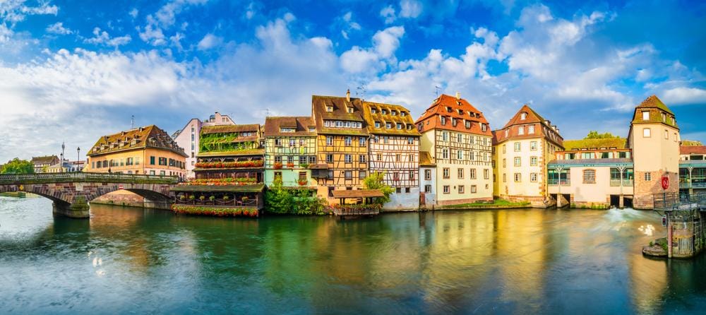 Fachwerkhäuser am Fluss in Straßburg, Frankreich, mit blauem Himmel und Brücke.
