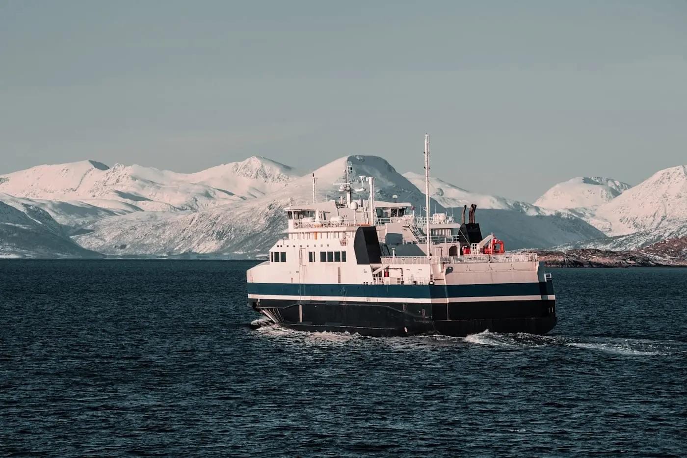 Fähre vor schneebedeckten Bergen, Norwegen, ruhige See und klare Winterluft.