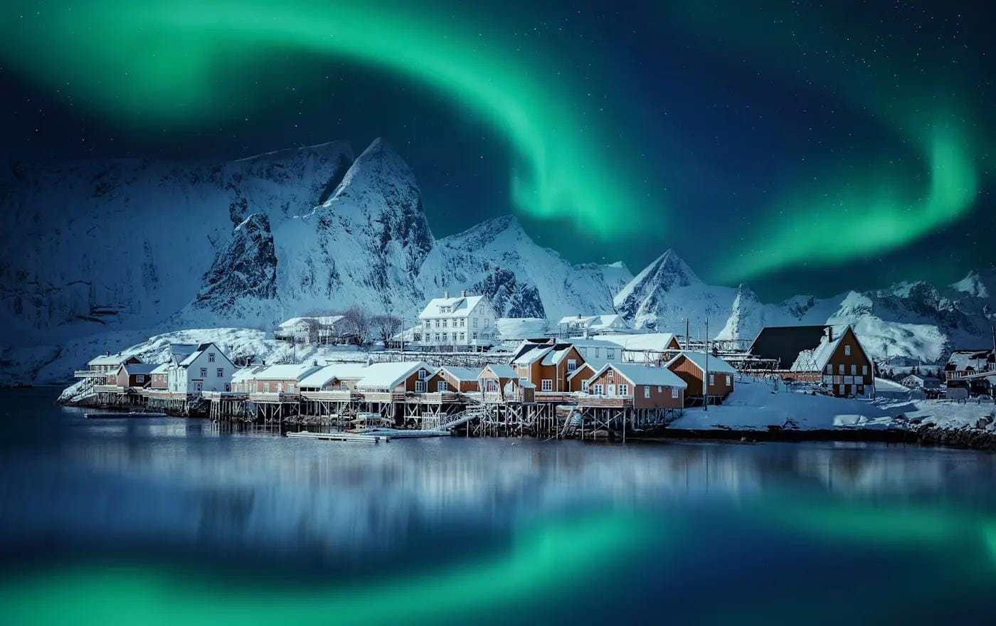 Norwegen, Lofoten: Schneedörfer vor Bergen, Nordlichter leuchten am Himmel.