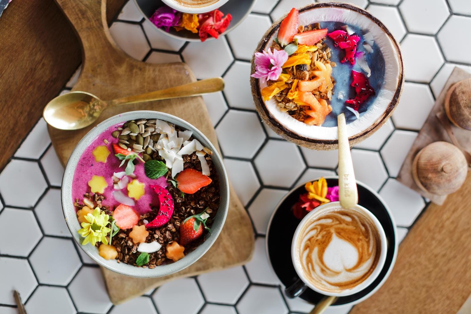 Bunte Smoothie-Bowls und Cappuccino auf stilvollem, weißem Fliesenhintergrund.
