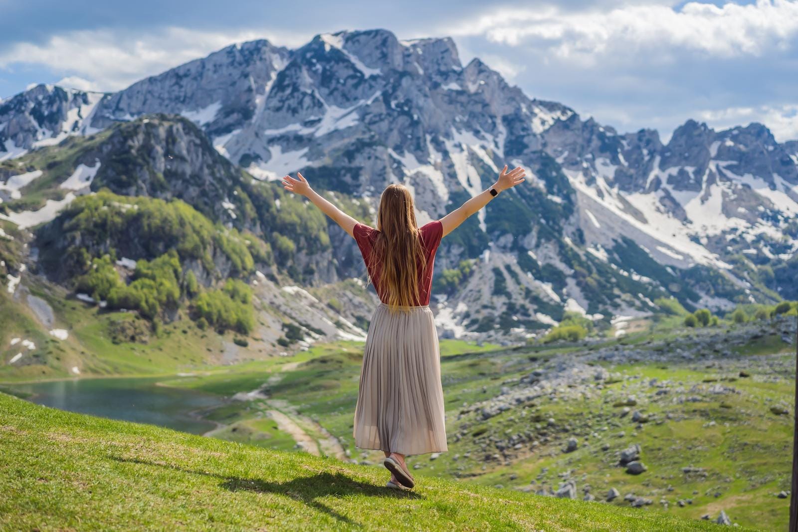 Frau mit erhobenen Armen blickt auf schneebedeckte Berglandschaft im Sonnenschein.