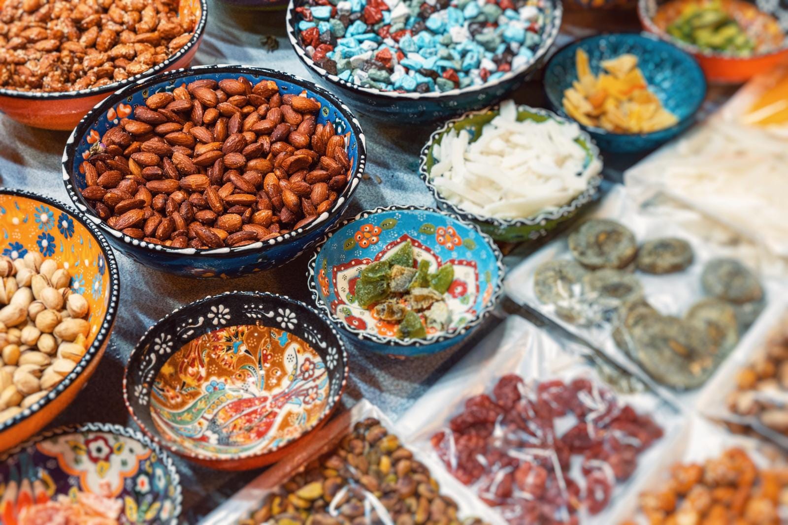 Bunte Schalen mit Nüssen, Trockenfrüchten und Süßigkeiten auf einem Marktstand.