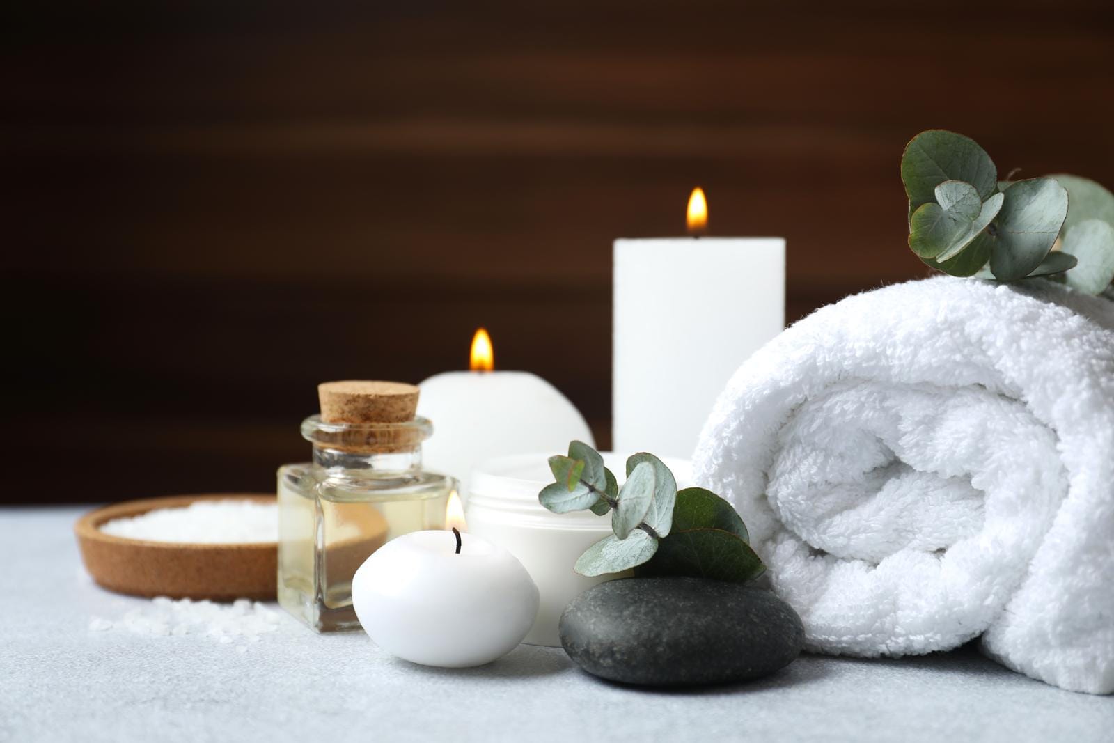 Spa-Ambiente mit Kerzen, handtuch, Öl und Eukalyptus auf einem grauen Tisch.