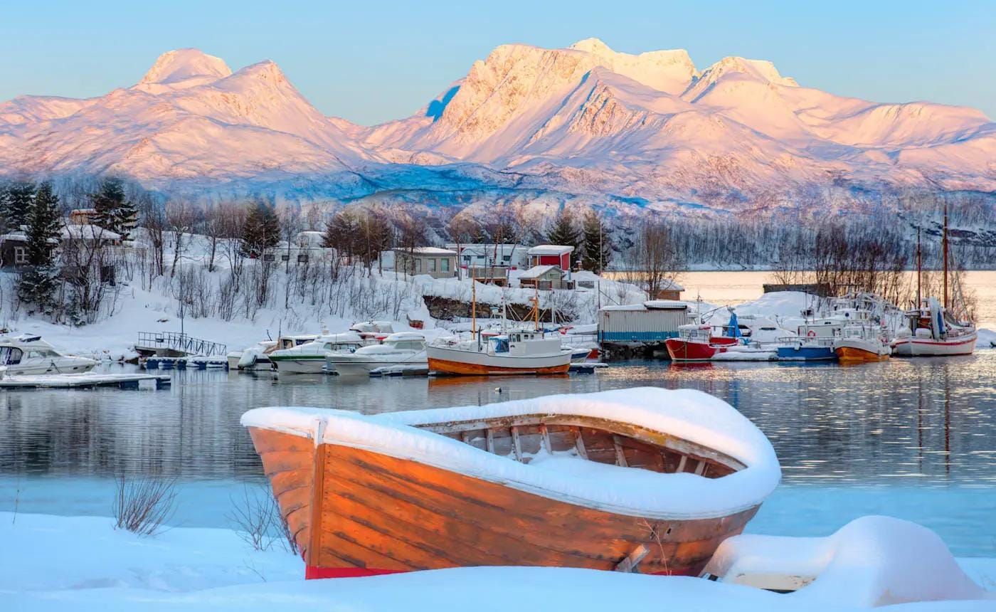 Verschneite Hafenlandschaft in Norwegen mit bunten Fischerbooten vor Bergen im Abendlicht.