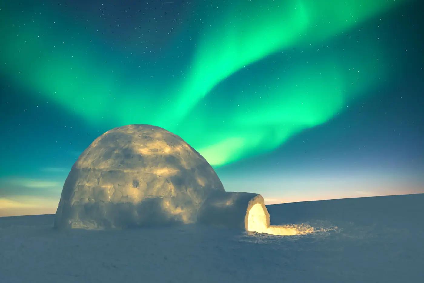 Iglo unter grünem Polarlicht in arktischer Landschaft bei Nacht.