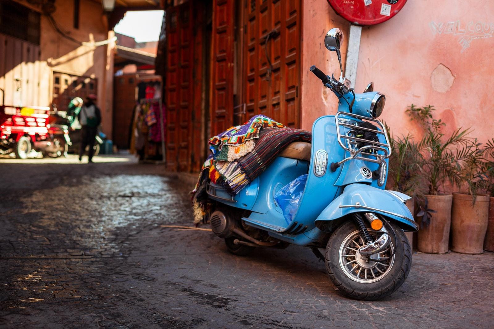 Blauer Motorroller mit bunten Decken in einer schmalen, sonnigen Straße in Marokko.