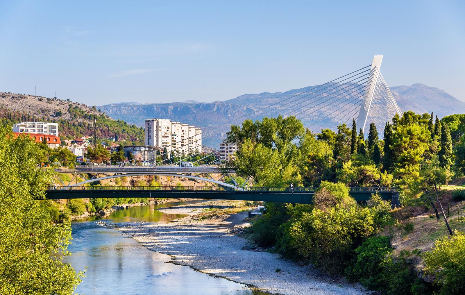Moderne Brücke und Fluss in Podgorica, Montenegro, umgeben von grüner Natur.