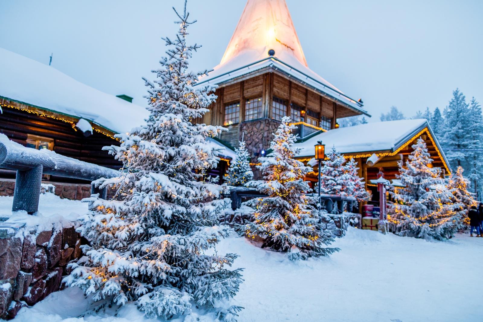 Schneebedeckte Holzhütte in Lappland, umgeben von beleuchteten Tannenbäumen.