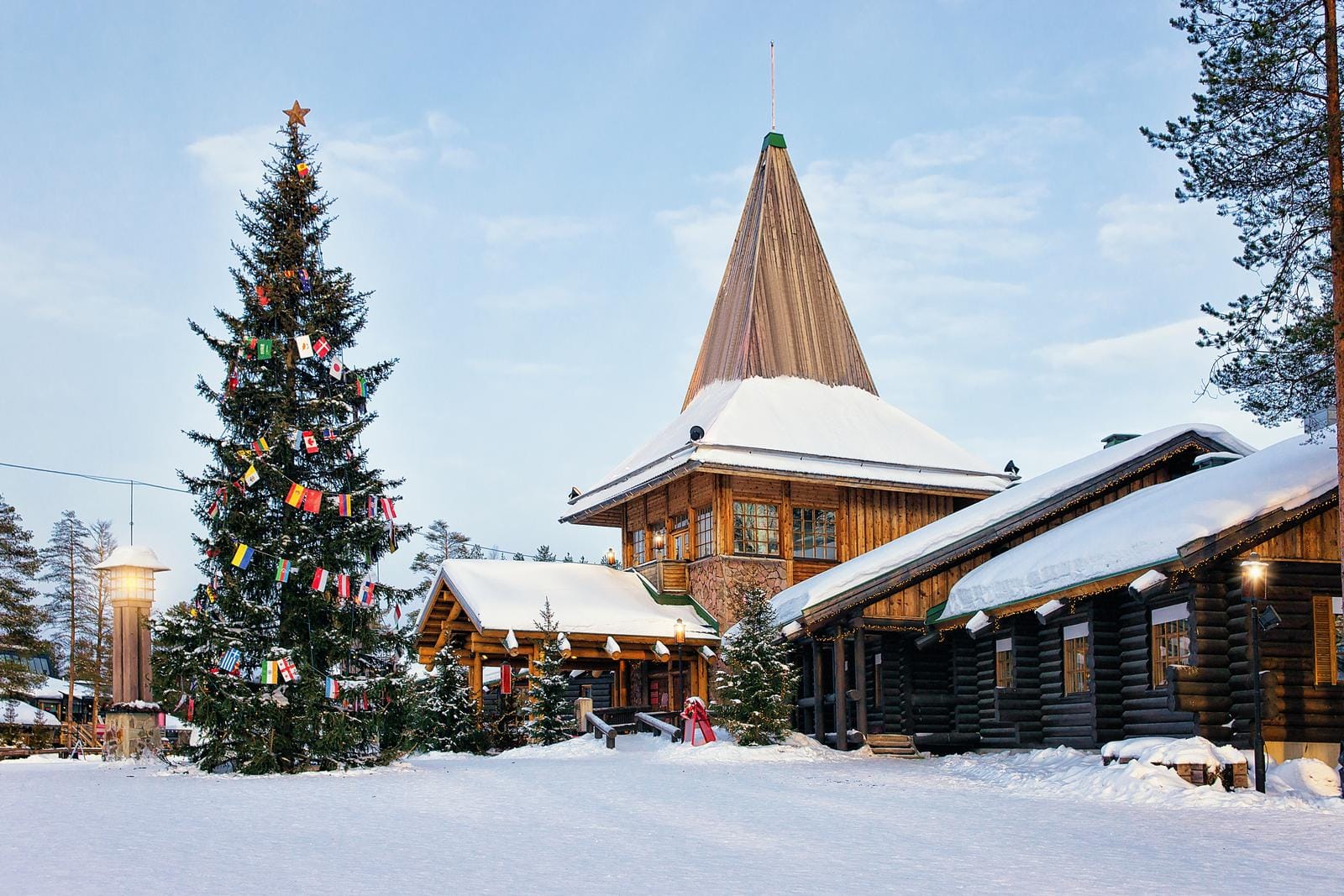 Verschneites Weihnachtsdorf in Finnland mit großem geschmücktem Tannenbaum und Holzhäusern.