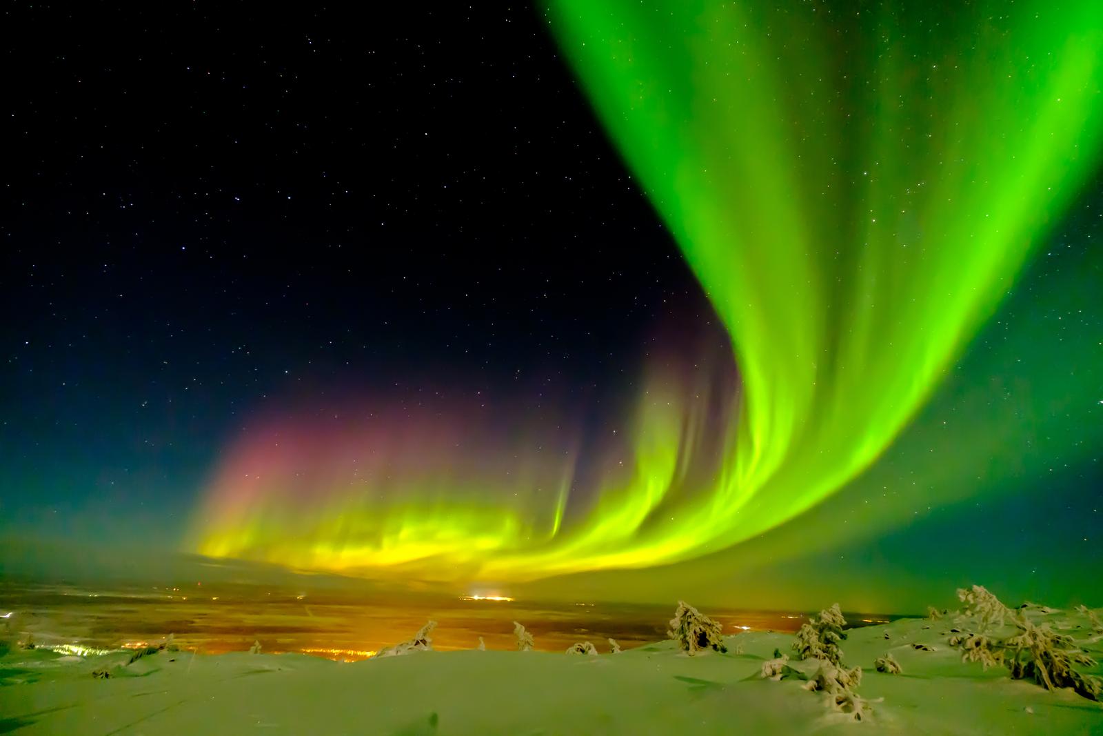 Nordlicht über verschneiter Landschaft, bunte Lichter am klaren Sternenhimmel.
