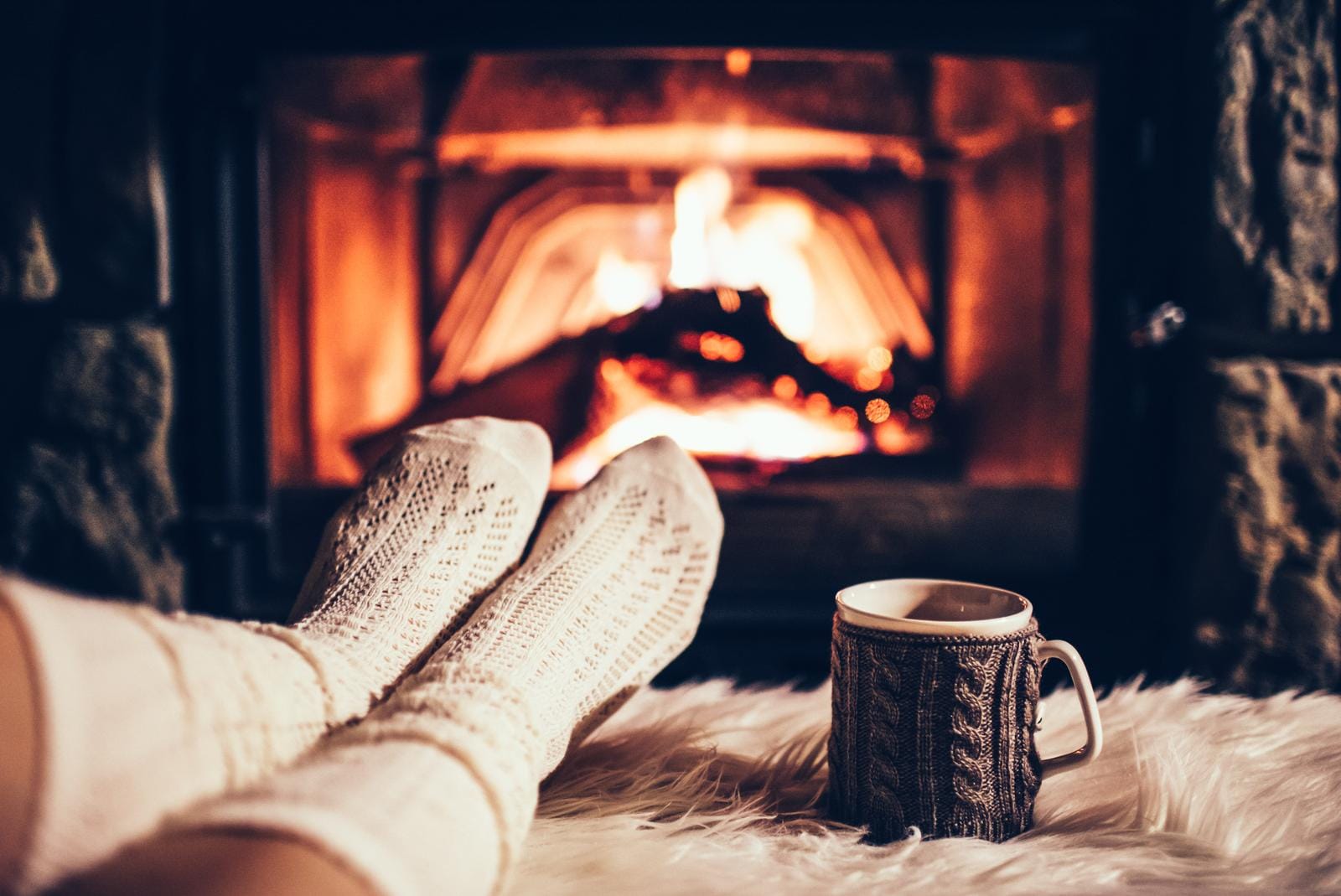 Gemütliche Atmosphäre vor Kamin mit Wollsocken und Tasse auf weichem Fellteppich.