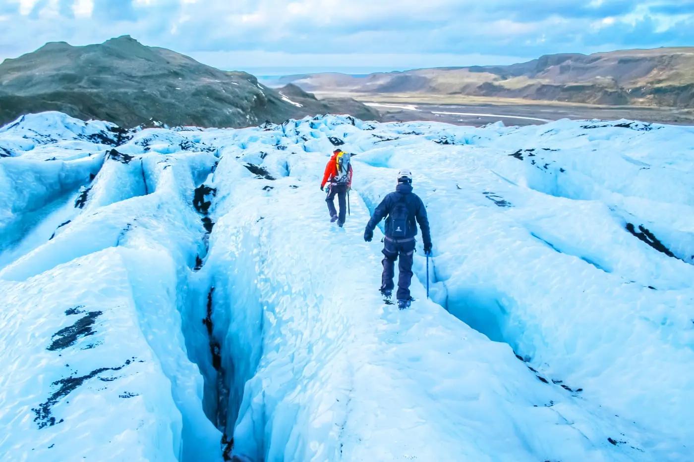 Zwei Personen wandern über einen blauen Gletscher in Island bei klarem Himmel.
