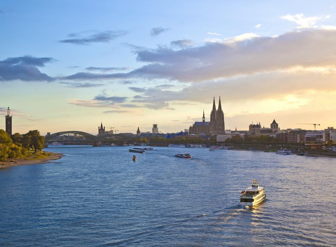 Der Rhein bei Köln mit Blick auf den Dom im Abendlicht, Boote auf dem Wasser.