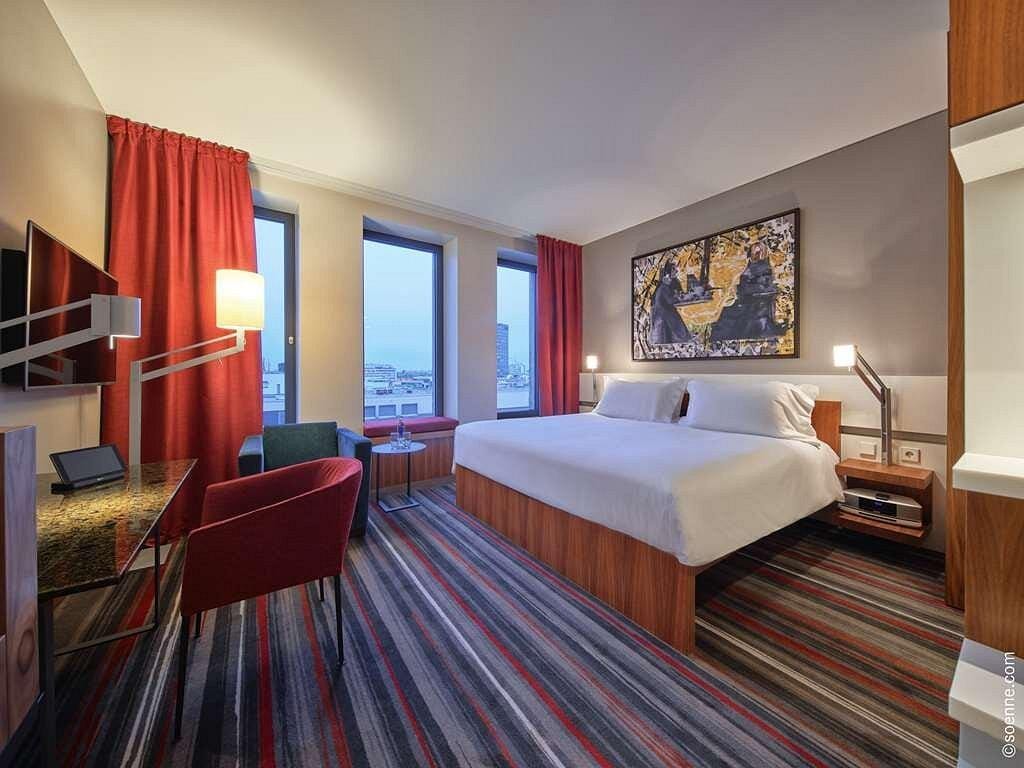 Modernes Hotelzimmer mit Doppelbett, rotem Vorhang, Gemälde an der Wand und Stadtblick.