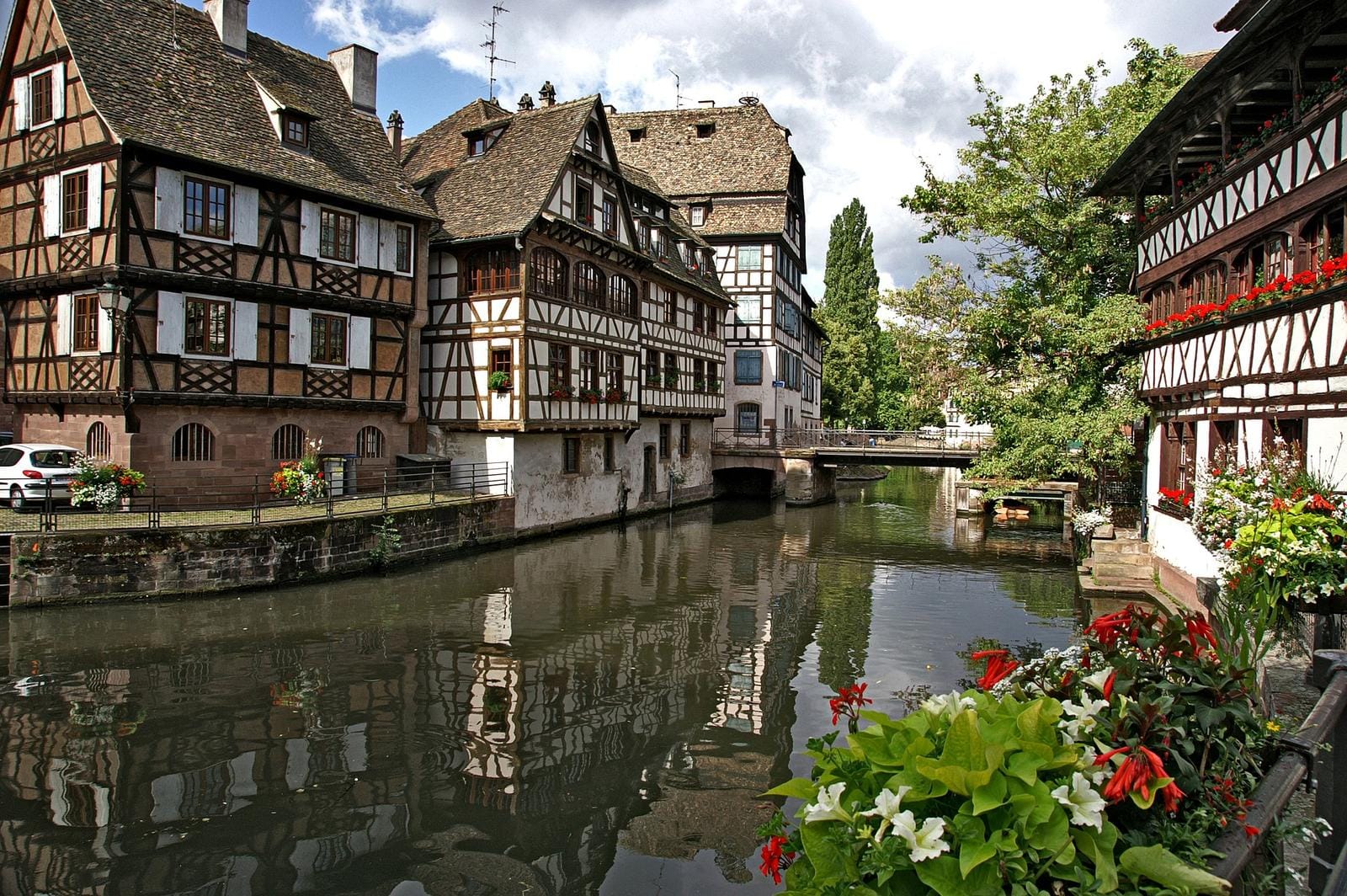 Fachwerkhäuser am Kanal in Straßburg, Frankreich, mit Blumen und Brücke.