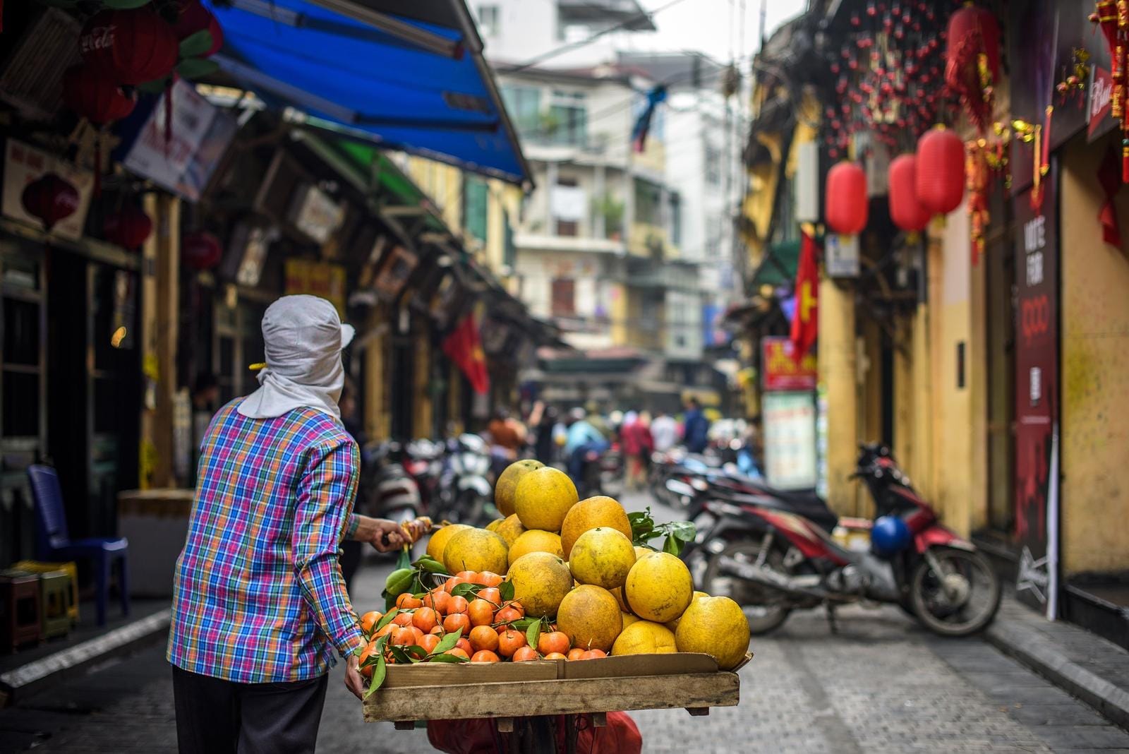 Händler mit Früchtewagen in belebter Altstadtgasse von Hanoi, Vietnam, mit Laternen.