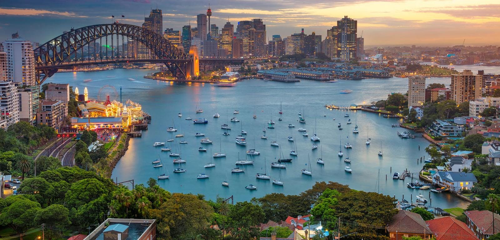 Blick auf Sydney Harbour Bridge und Skyline bei Sonnenuntergang, Australien, Boote im Hafen.