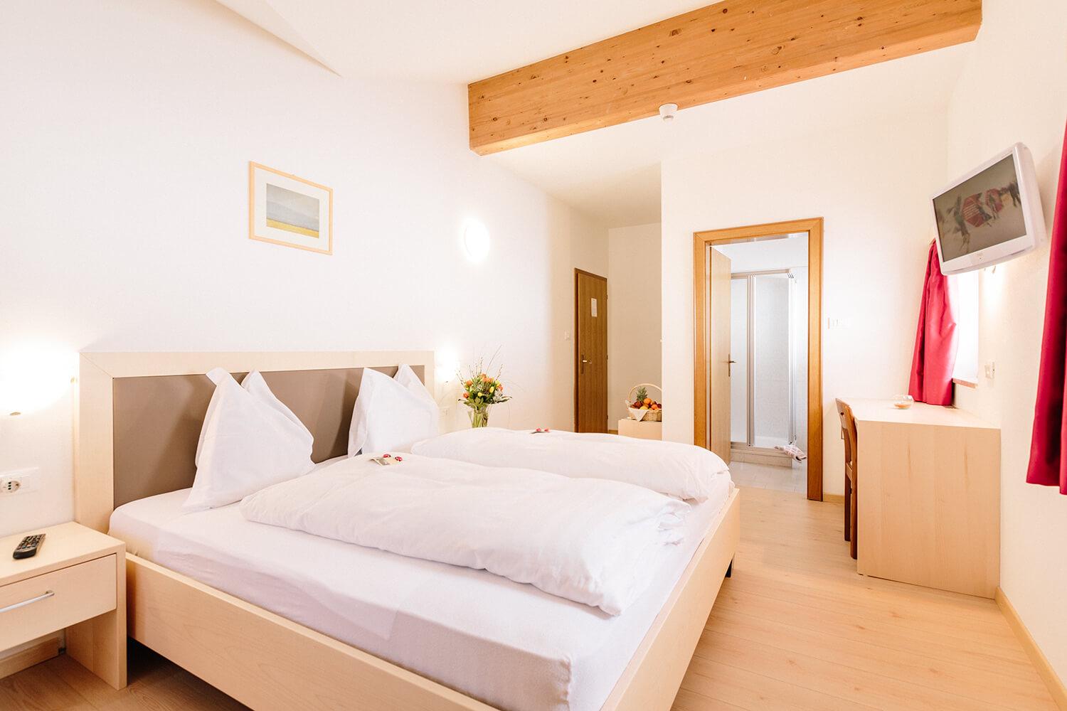 Helles Hotelzimmer mit Holzmöbeln, Blumen und gemütlichem Doppelbett.