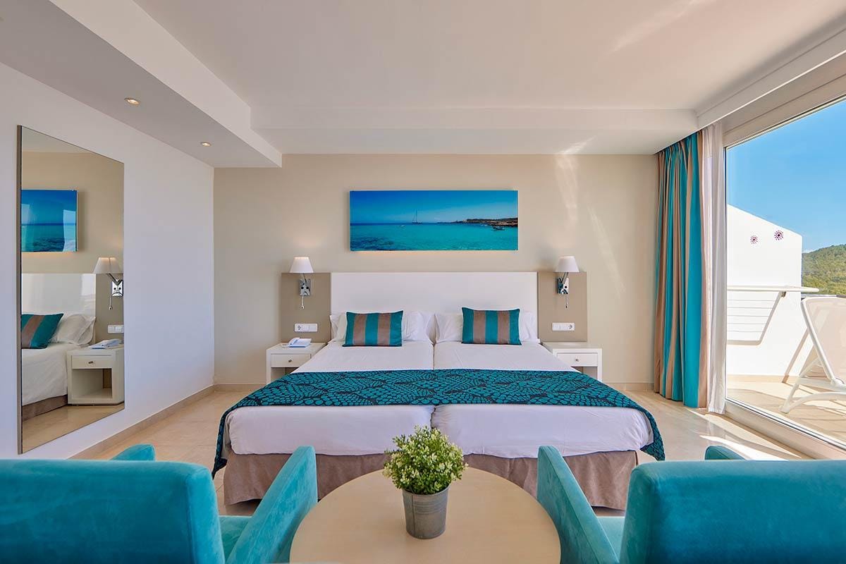 Modernes Hotelzimmer mit Doppelbett, türkisfarbenen Kissen und Meerblick.