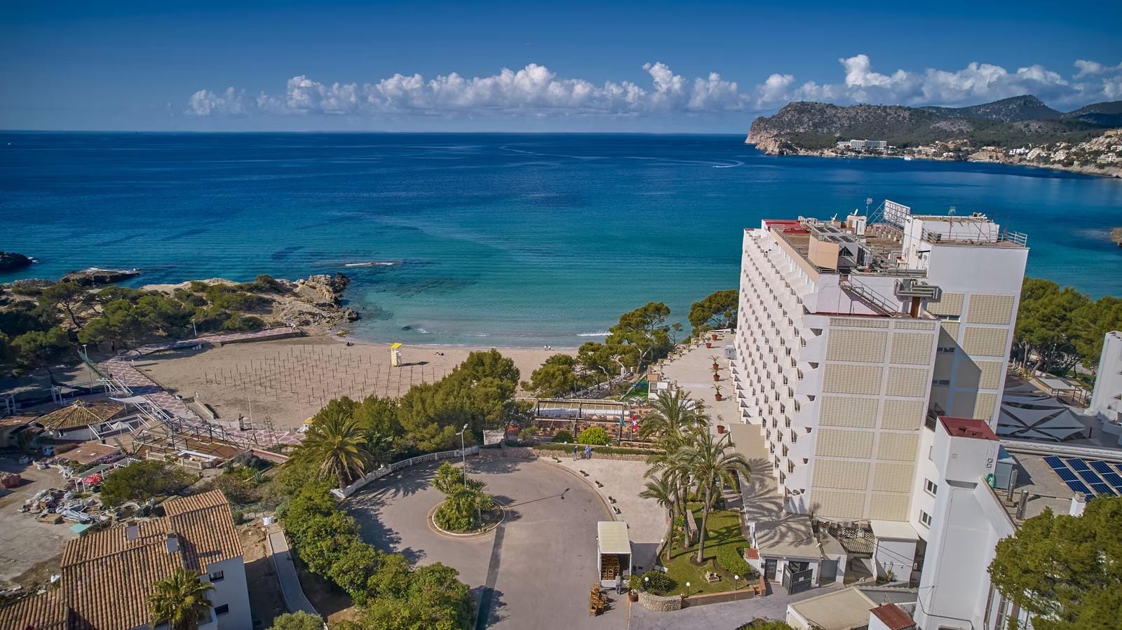 Küstenhotel auf Mallorca neben Sandstrand, umgeben von Pinien und türkisblauem Meer.