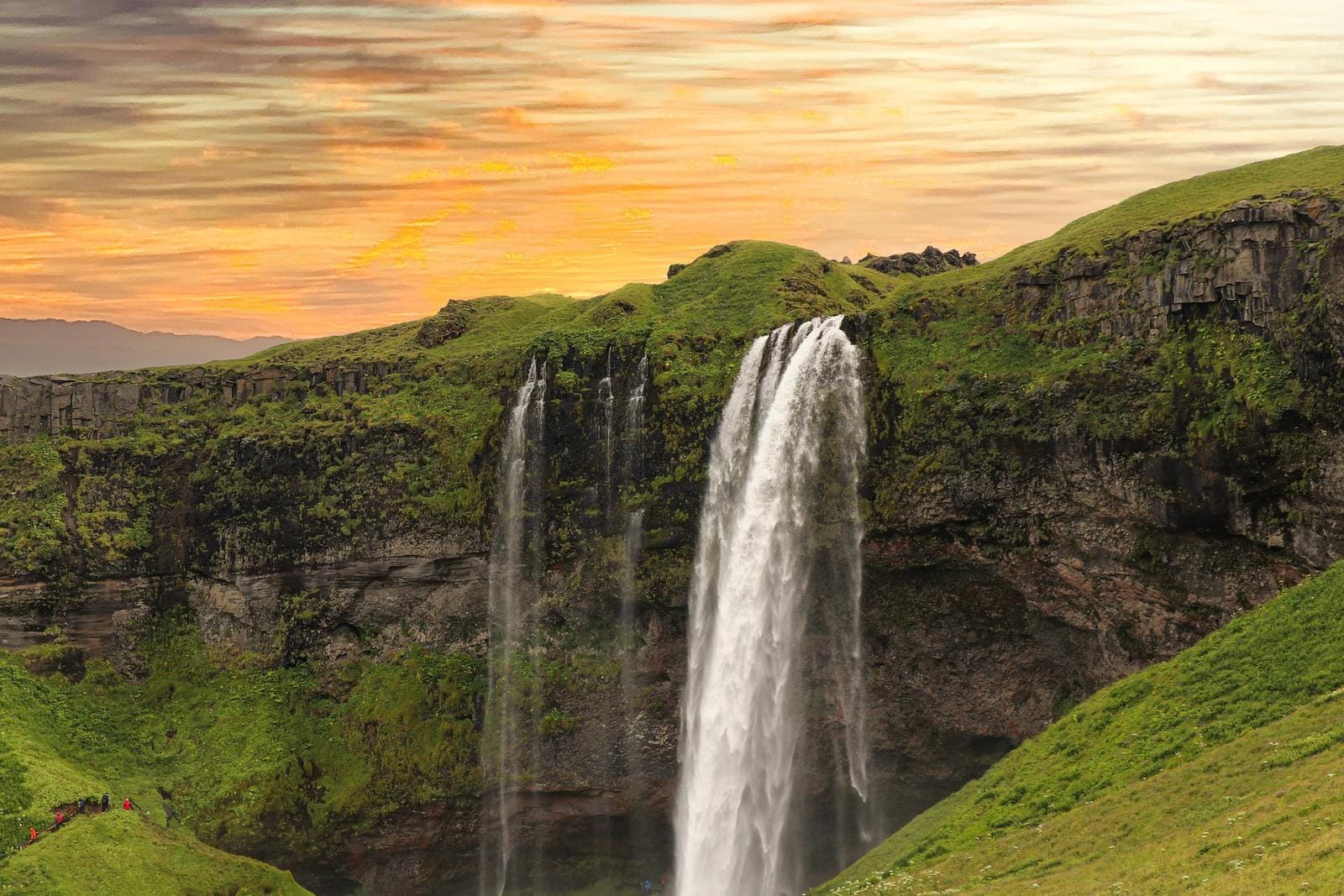 Spektakulärer Wasserfall in Island bei Sonnenuntergang, umgeben von grüner Landschaft.