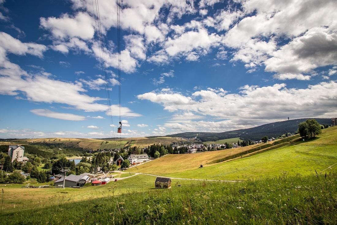 Landschaft in Oberwiesenthal, Deutschland, mit Seilbahn und grünen Hügeln unter blauem Himmel.