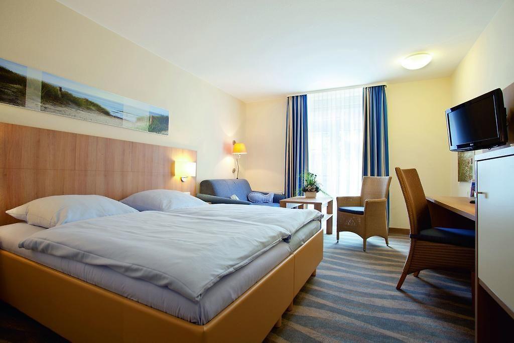 Helles Hotelzimmer mit Doppelbett, blau-gelbem Dekor, Schreibtisch und Sitzecke.