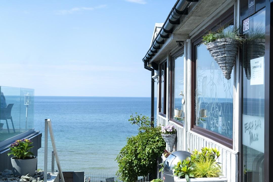 Haus am Meer mit großen Fenstern, Küstenblick, blauer Himmel, Sonnenlicht.