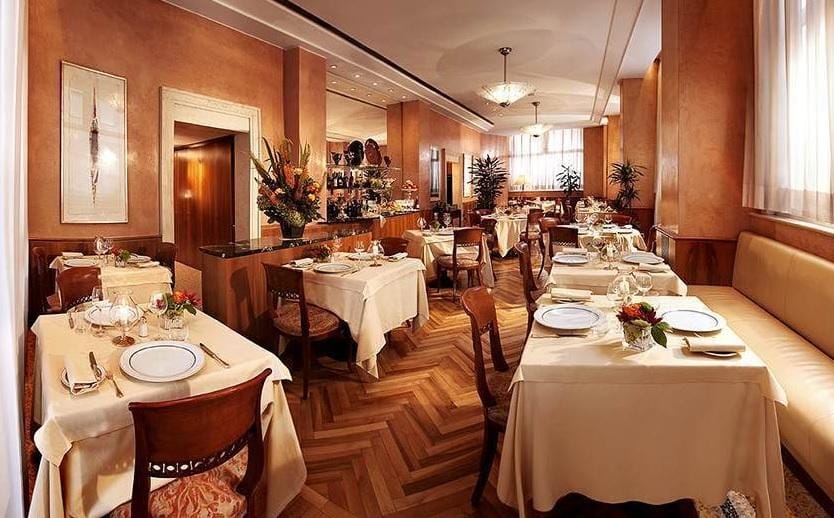 Elegantes Hotelrestaurant mit Parkettboden, gedeckten Tischen und warmen Erdtönen.