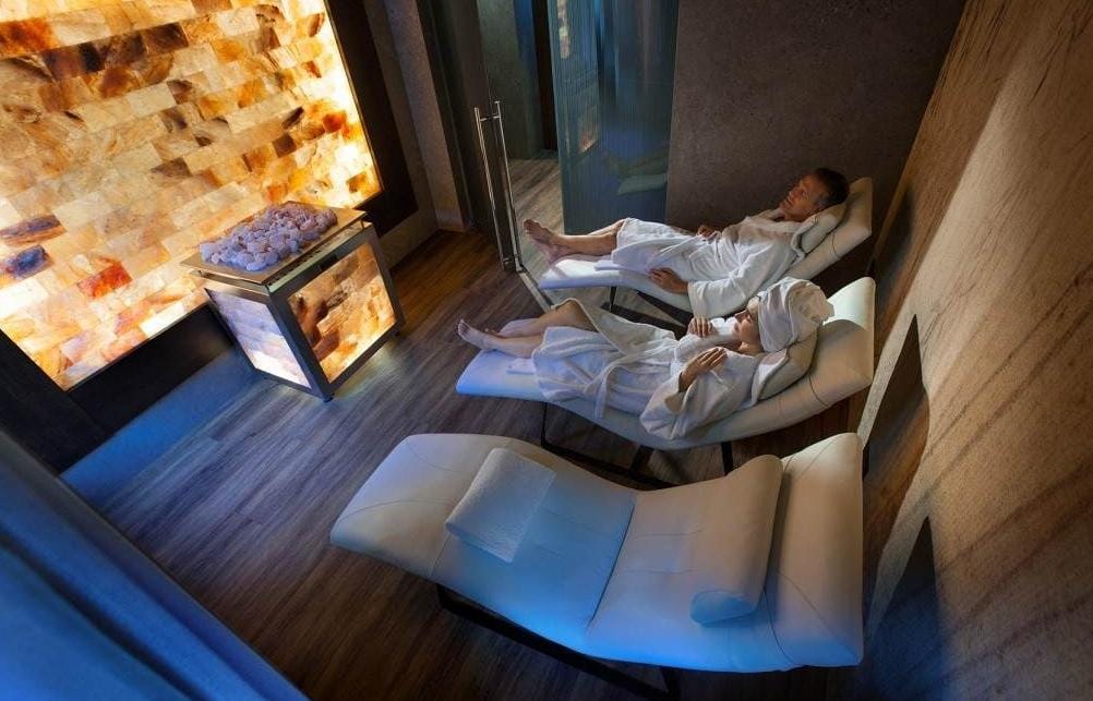 Gemütlicher Spa-Raum mit Salzsteinwand und weißen Liegen im gedämpften Licht.