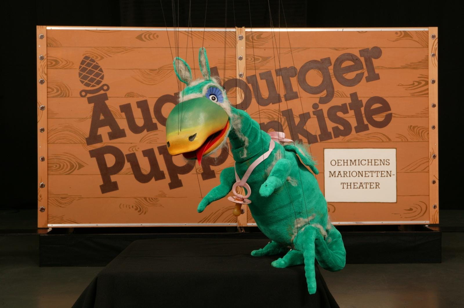 Grüner Drache im Augsburger Puppenkiste-Theater, Hintergrund Holzkiste.
