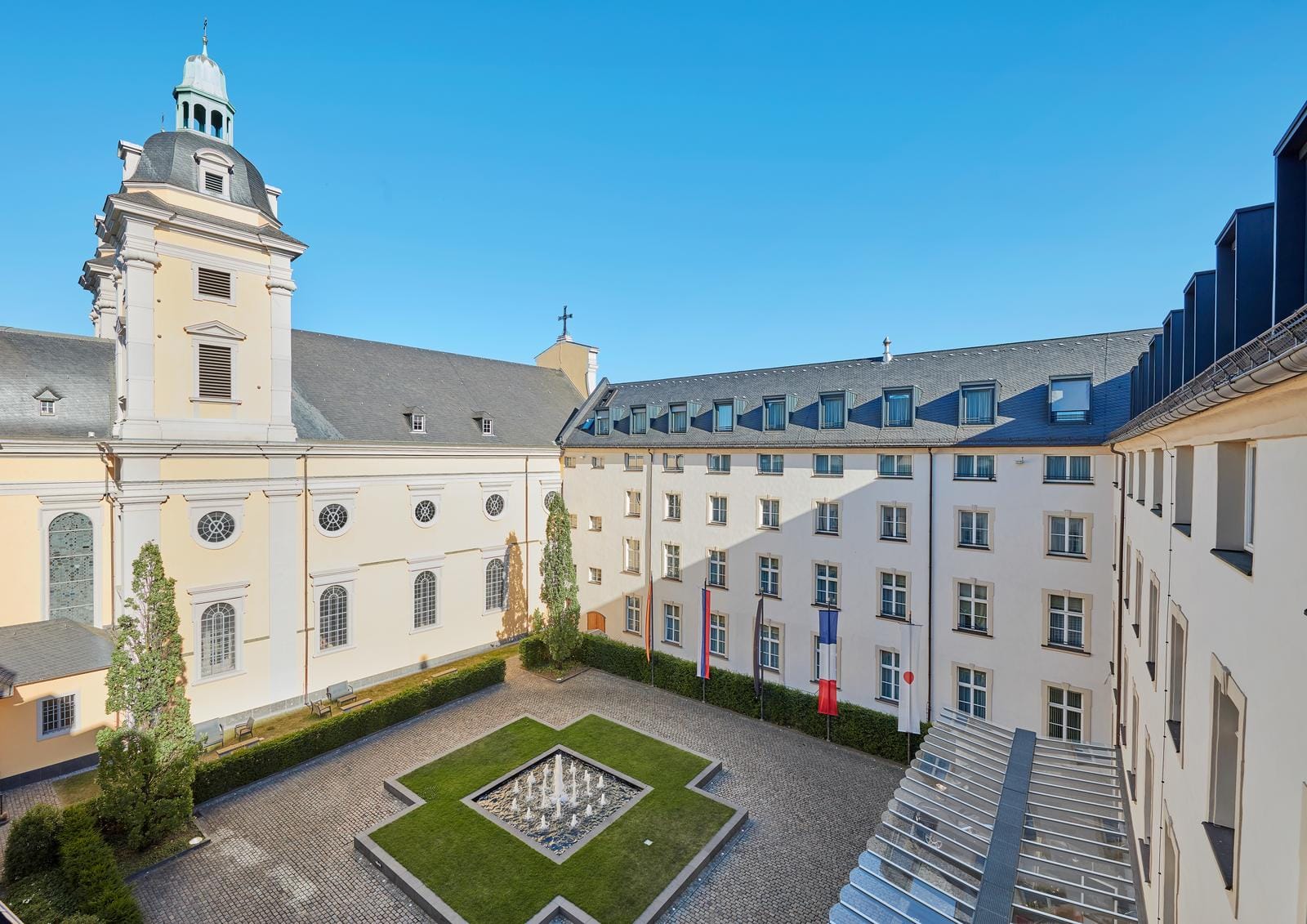 Historisches Gebäude mit gelber Fassade, zentraler Hof, Brunnen, blaue Flaggen.