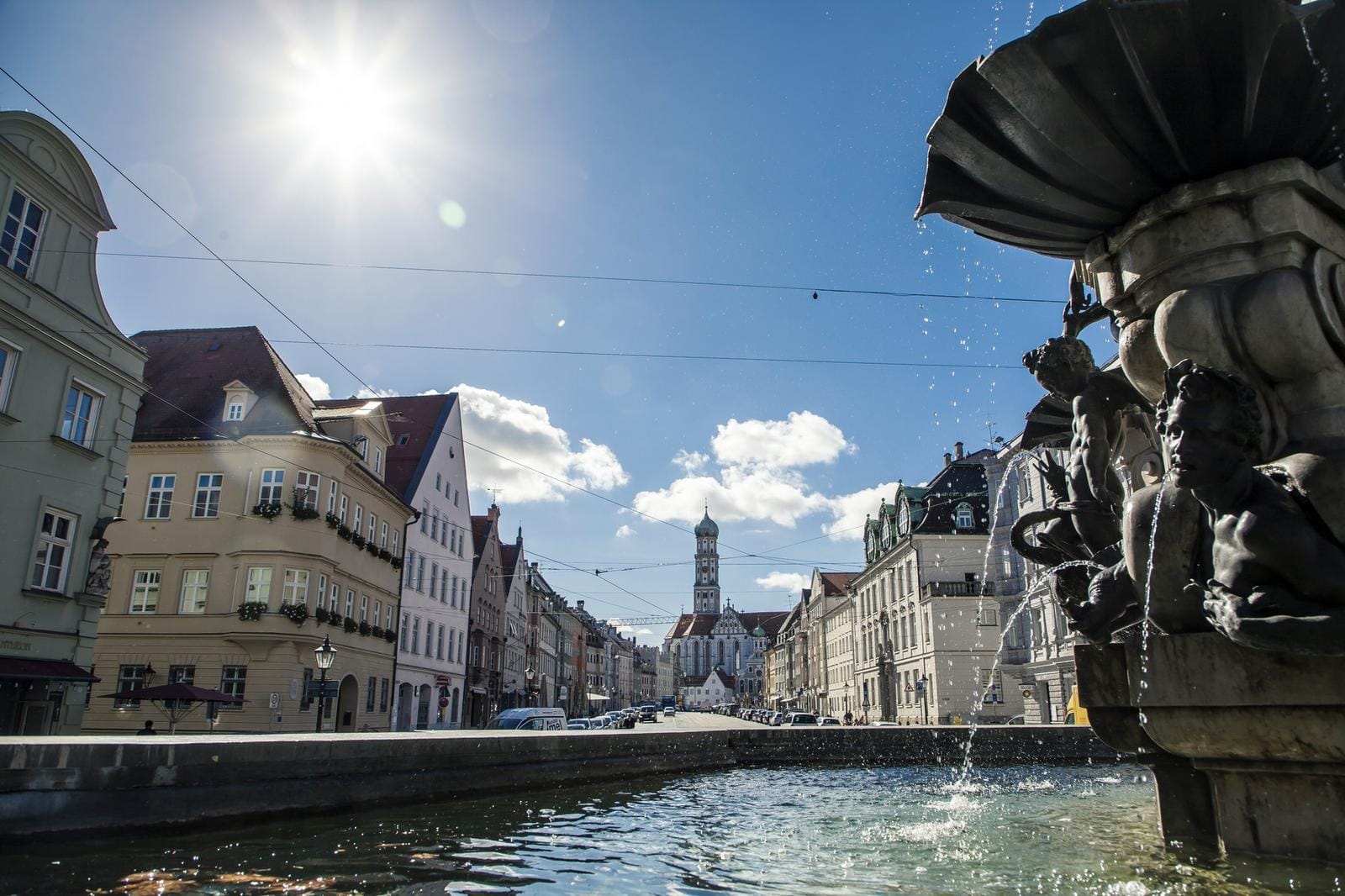 Brunnen und historische Fassaden, Augsburg, bei Sonnenschein und blauem Himmel.