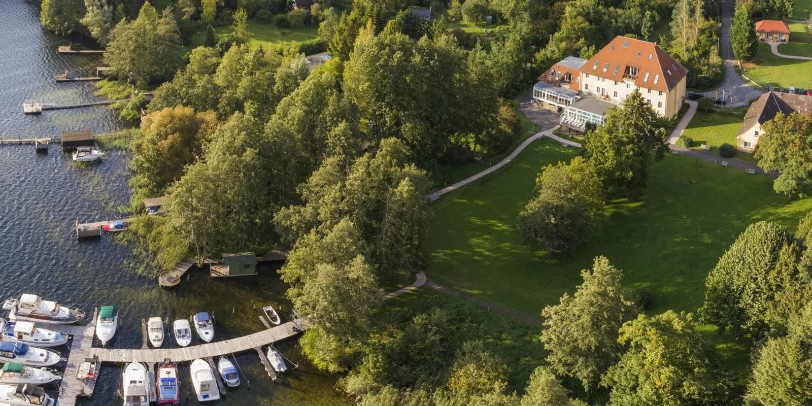 Luftbild von Hotelanlage am See, umgeben von grünen Bäumen und Bootsanlegestellen.