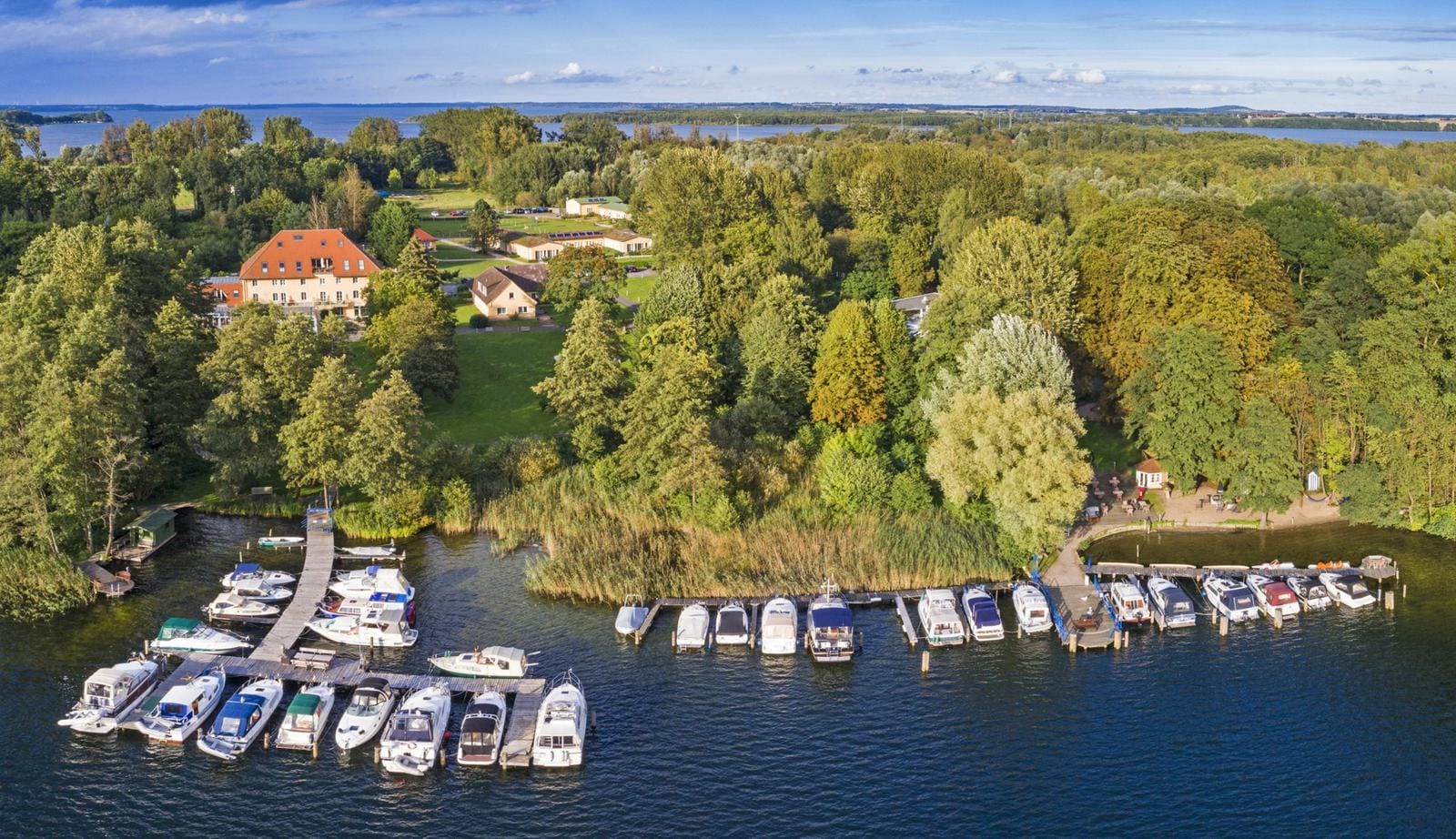 Landschaft in Deutschland mit Hafen, Booten, grünem Wald und einem roten Hausdach.