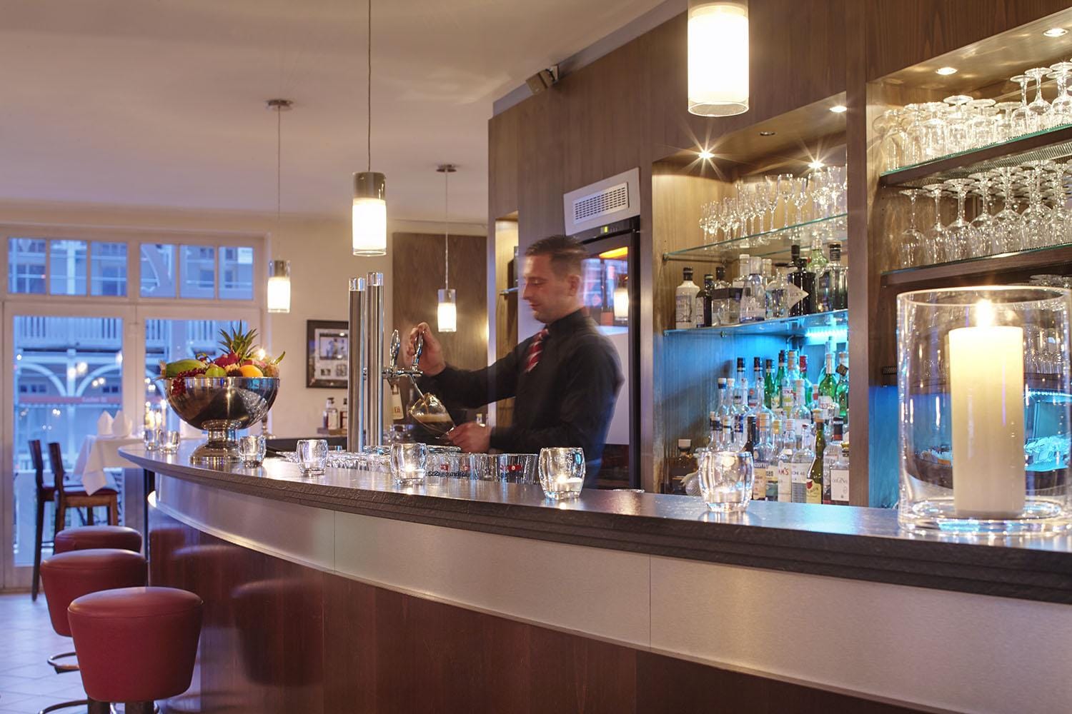 Hotelbar mit moderner Holzoptik, gedämpfte Beleuchtung, Barkeeper und Getränkekühler.