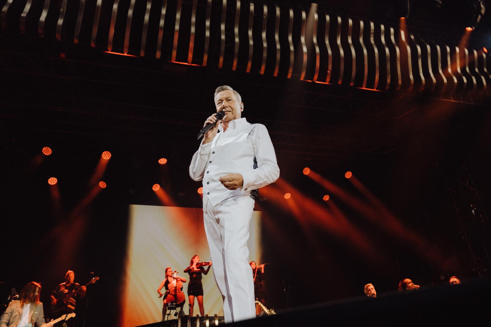 Bühne mit Sänger in weißem Anzug, rotes Licht, Musiker im Hintergrund.